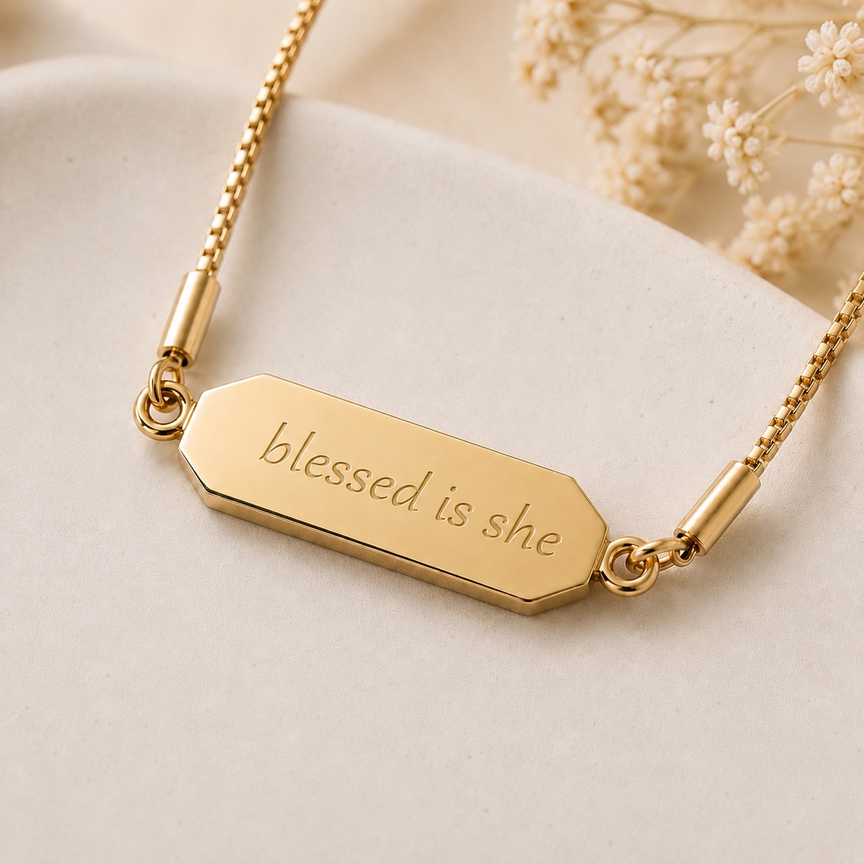 Gold necklace with 'blessed is she' engraving on a beige background