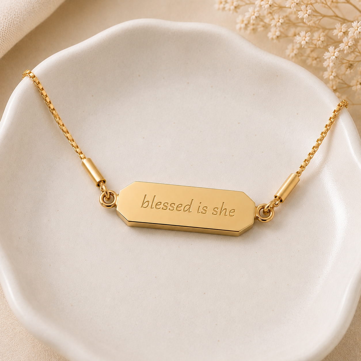 Gold necklace with 'blessed is she' pendant on a white dish
