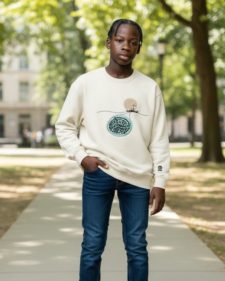 Person wearing a white sweatshirt with a graphic design, standing on a path in a park.