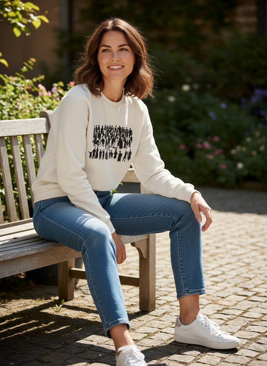 Woman sitting on a bench wearing a white sweatshirt with black graphics and blue jeans, surrounded by greenery.