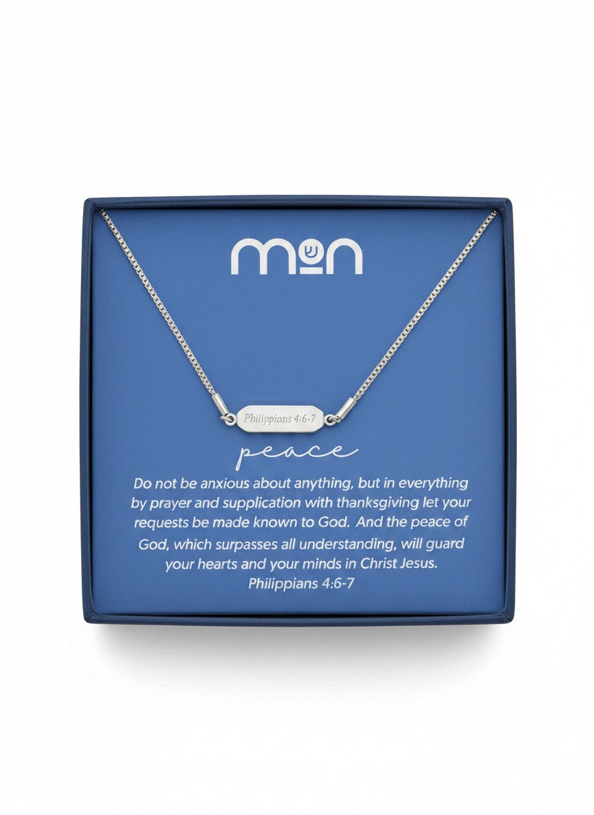 Silver necklace with 'Philippians 4:6-7' on the back of the pendant, placed on a blue card with 'mon' branding in a black box
