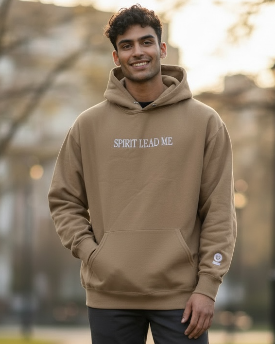 Man wearing a brown hoodie with text, standing on a path in a park.