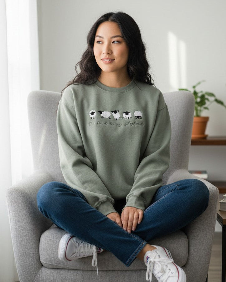 Woman sitting on a chair wearing a green sweatshirt with a graphic design.