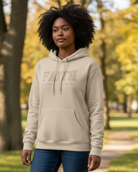Person wearing a beige hoodie with 'FAITH over fear' printed on it, standing in a park.