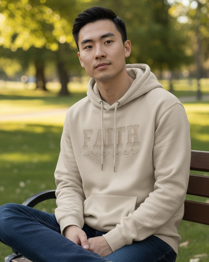 Man sitting on a bench in a park wearing a beige hoodie that reads faith over fear