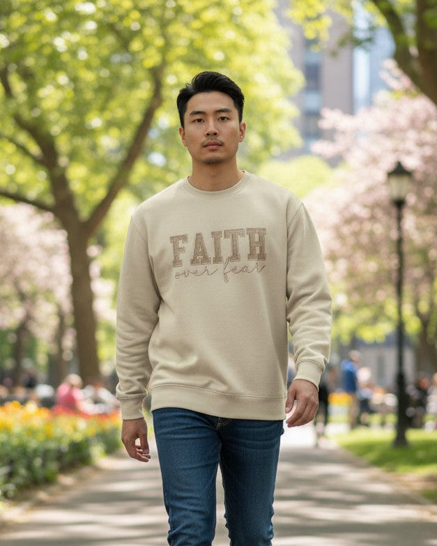 Man walking in a park wearing a beige sweatshirt with 'FAITH' text