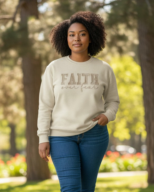 Woman wearing a beige sweatshirt with 'Faith over Fear' text, walking in a park.