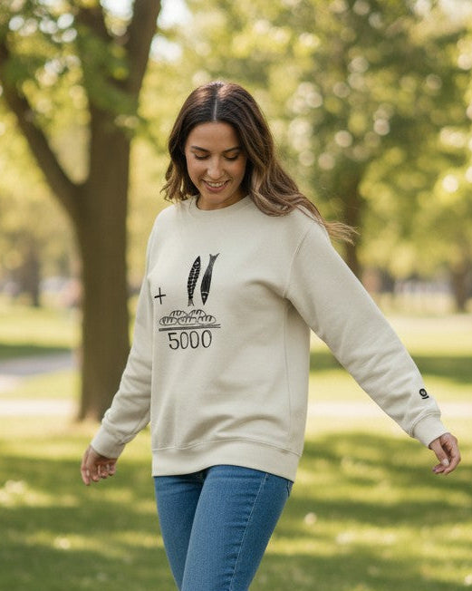 Woman walking in a park wearing a beige sweatshirt with text and blue jeans.