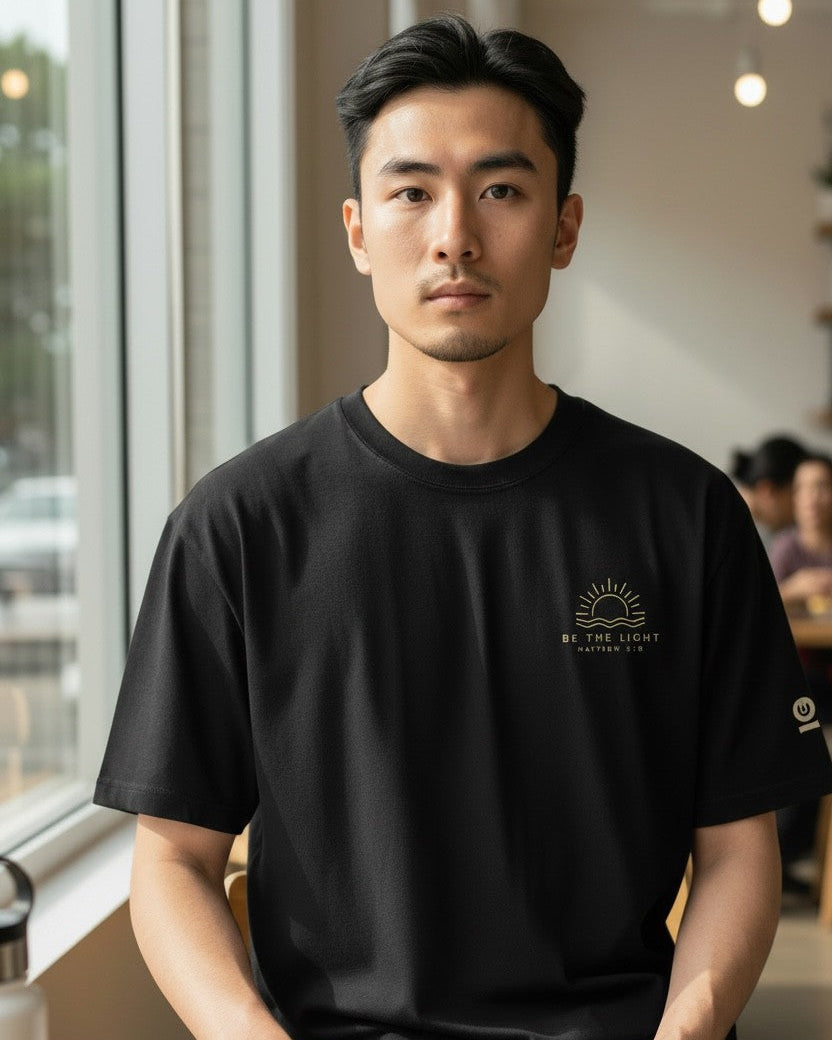 Man wearing a black t-shirt with a logo, sitting at a table with a book in a casual setting.